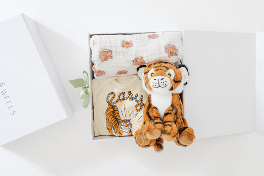 Baby gift set with tiger-themed items including a plush toy, blanket, and pillow on a white surface.