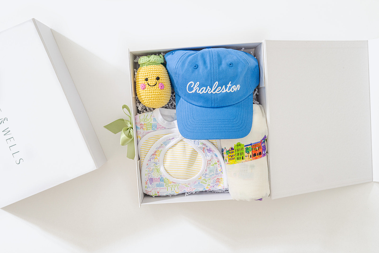 Gift set with a blue cap, pineapple plush toy, and baby bib in a box.