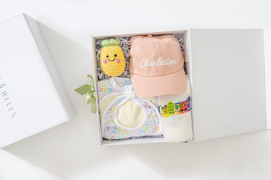 Gift set with a pink cap, plush toy, and baby blanket in a box on a white background