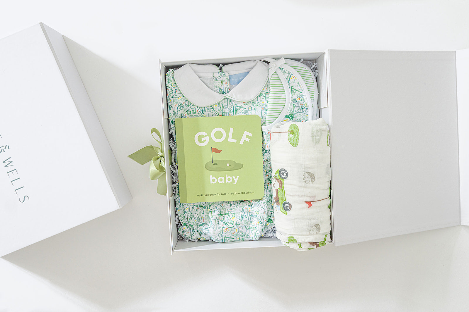 Decorative image open gift box with golf-themed baby dress, bloomers, and matching bib, golf-print swaddle blanket and "Golf Baby" board book. 