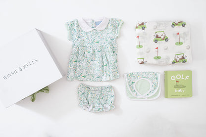 Decorative image layout of golf-themed baby dress, bloomers, and matching bib, golf-print swaddle blanket and "Golf Baby" board book. 