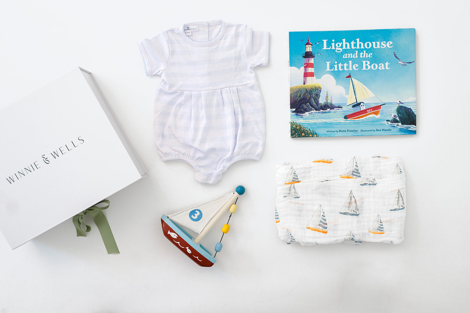 Decorative image of blue and white striped baby onesie, sail boat print swaddle blanket, wooden sailboat toy, and picture book